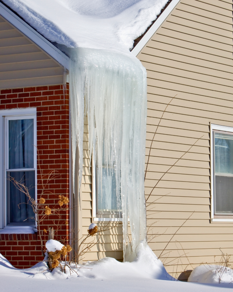 Photo d’un important barrage de glace descendant du toit jusqu’au mur d’une maison.