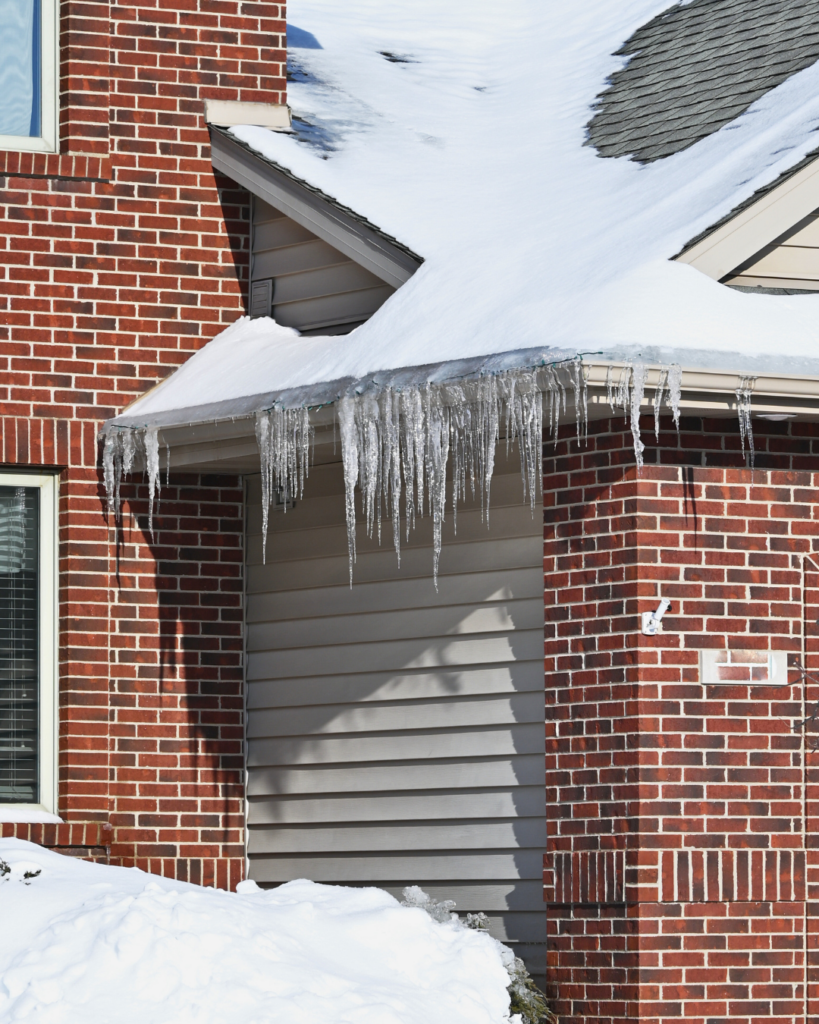 Photo d’un barrage de glace formé au bord d’un toit enneigé d’une maison.